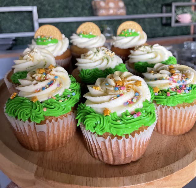 Cupcakes with green and cream swirled frosting, rainbow sprinkles, gold stars and a cookie on top, on a wooden stand