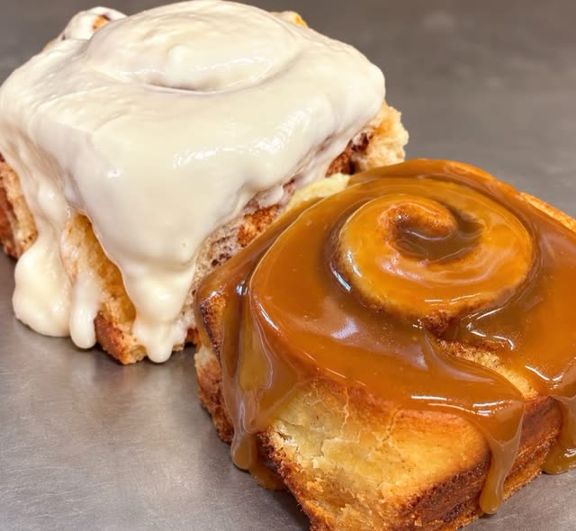 Two cinnamon rolls side by side, one covered in white icing and one in caramel